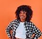 Portrait of a smiling woman in trendy attire, posing against an orange backdrop with confidence and style.
